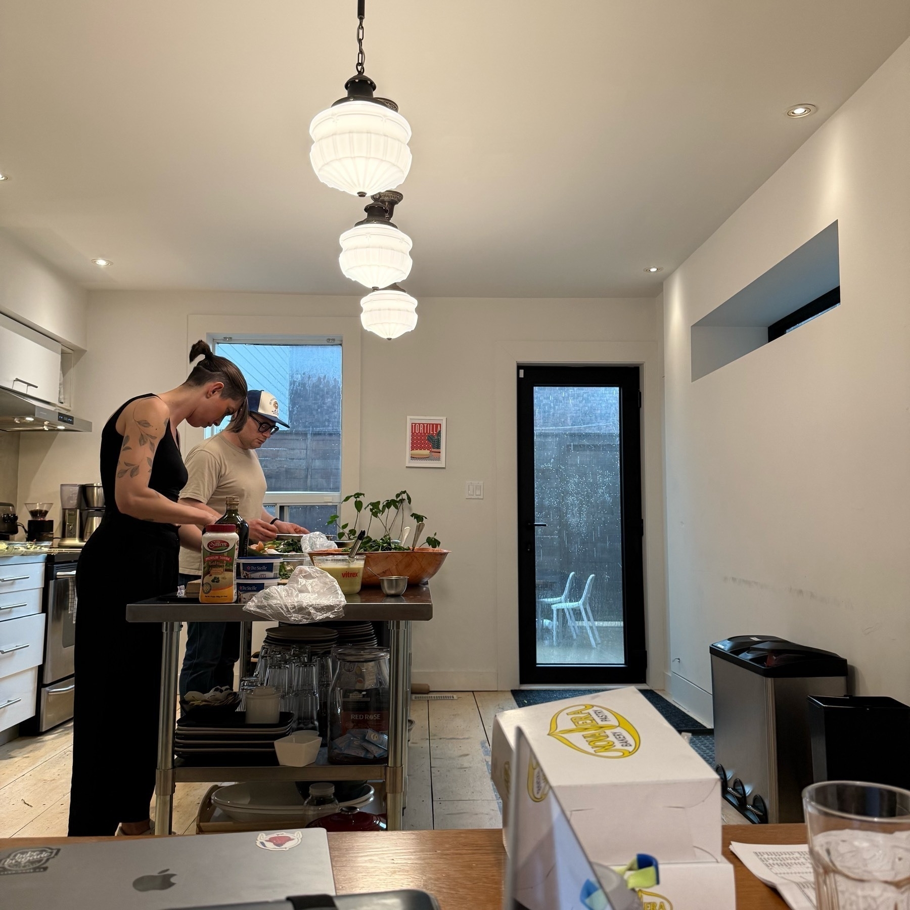 Two awesome people, Serena and Max, making dinner at a long table. In the background there is a big rain storm.