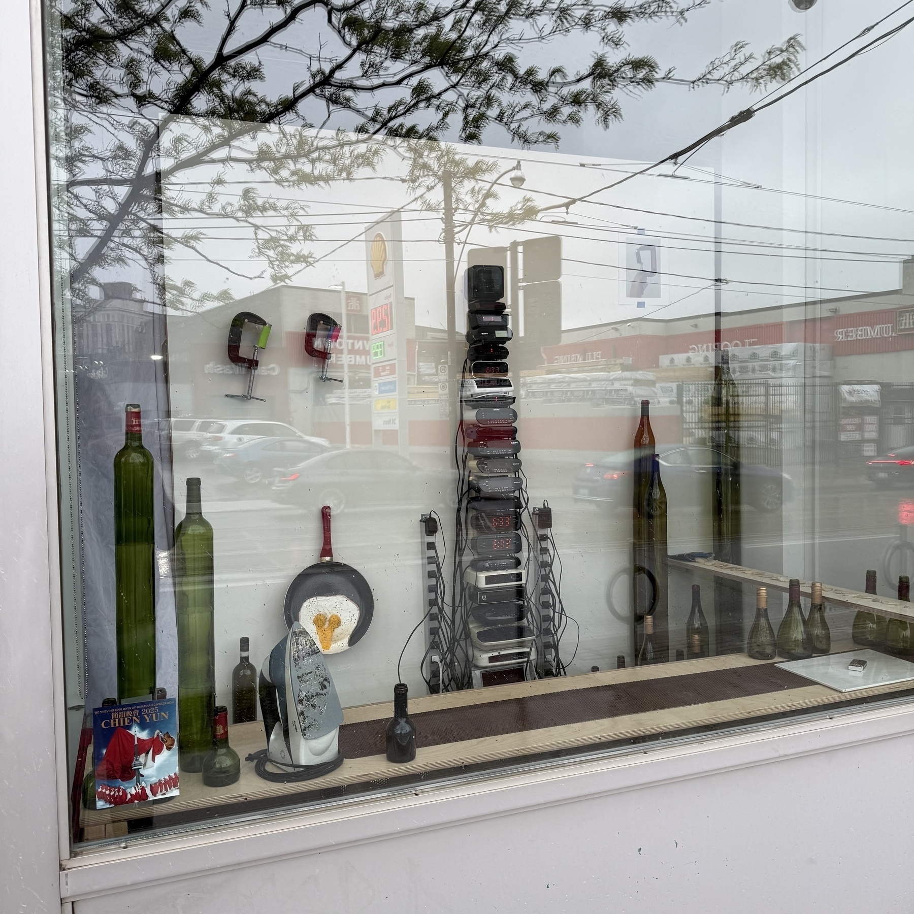 A storefront window display features various bottles and decorative items, with reflections of the street and trees visible on the glass.