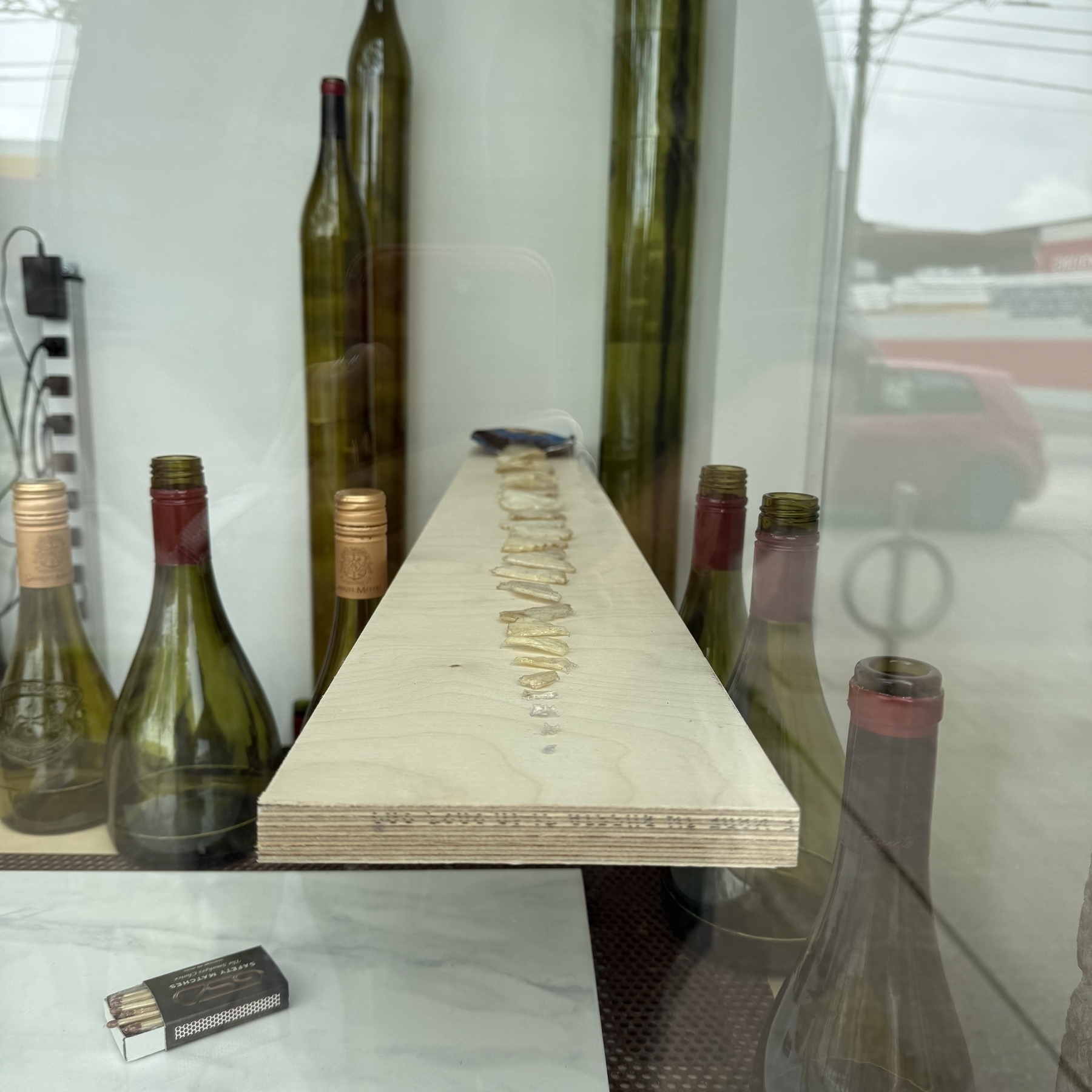 Several wine bottles, a pack of matches, and a lineup of a chips ordered by size are displayed near a window.